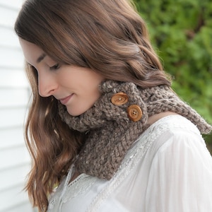 May include: A brown knitted cowl neck scarf with two wooden buttons. The scarf is worn by a person with long brown hair.