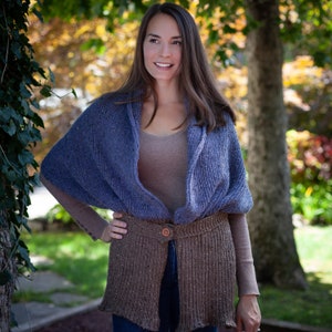 May include: A blue and brown knitted shawl with a button closure. The shawl is worn over a brown tank top and blue jeans.