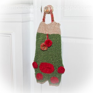 May include: A handmade Christmas stocking in green, tan, and red, hanging from a door handle. The stocking features a knitted design with red pom-poms and a loop for hanging. The top is tan, the body is green, and the accents are red.