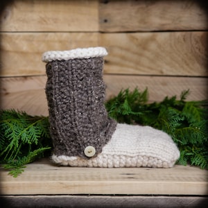 May include: A pair of knitted slippers with a brown cuff and a white sole. The slippers have a button on the cuff.