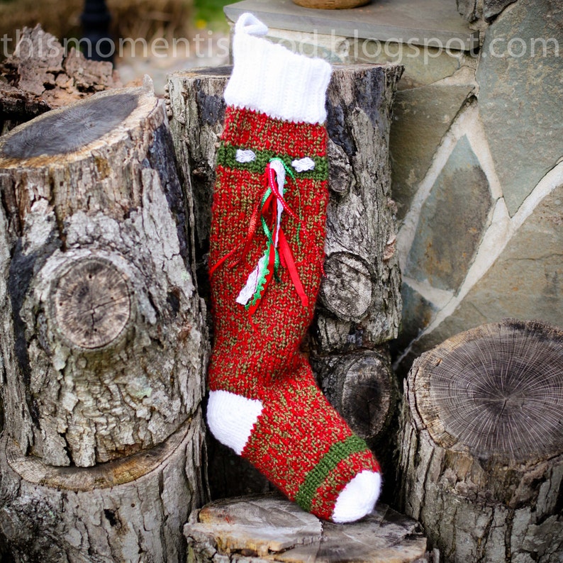Peut inclure: Une chaussette de No&euml;l rouge et verte en tricot avec des bordures blanches et un revers blanc. La chaussette est orn&eacute;e de rubans verts et rouges et est accroch&eacute;e &agrave; une souche d'arbre.