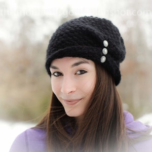 Puede incluir: Un gorro de punto negro con un ajuste holgado y detalles de botones plateados. El gorro lo lleva una persona con el pelo largo y castaño.