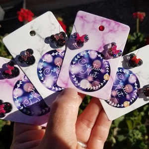 May include: Four pairs of black and pink glitter mouse head stud earrings on white cards with the text "Creative Nest" on each card.