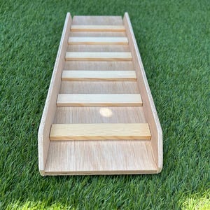 May include: A light-coloured wooden ramp featuring a series of evenly spaced horizontal slats attached to the surface. The structure has two raised side panels running the length of the ramp, constructed from plywood with a natural wood grain finish.