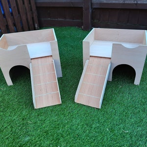 May include: Two wooden pet houses with ramps. The houses are light brown and have a small opening at the front. The ramps are made of wood and have a light brown finish.