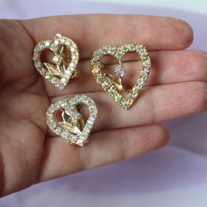 May include: A set of three gold-tone heart-shaped brooches with clear iridescent rhinestones and a floral design.