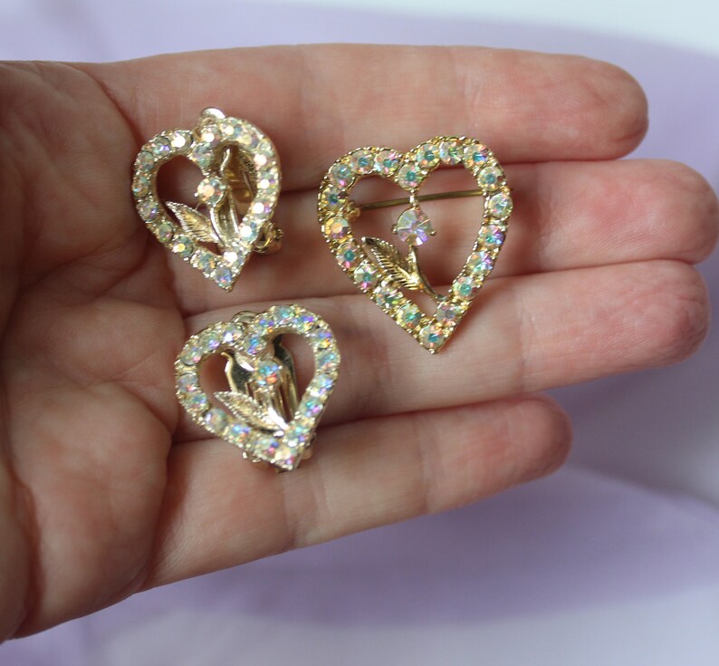 May include: A set of three gold-tone heart-shaped brooches with clear iridescent rhinestones and a floral design.