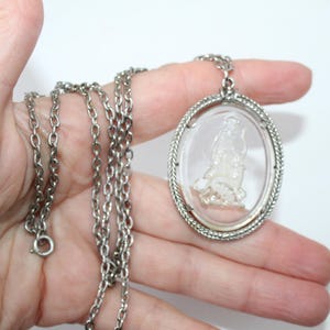 May include: Silver-toned necklace featuring an oval pendant with a clear, detailed cameo design. The pendant is framed with a textured border and hangs from a delicate chain. A classic piece of jewelry.