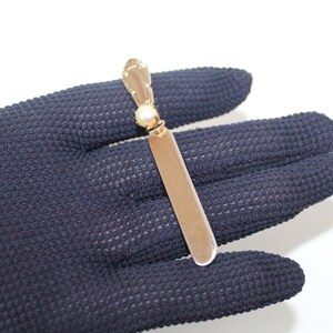 May include: A gold-colored butter knife with a pearl accent. The knife has a rectangular blade and a decorative handle. The pearl is set near the handle. The knife is displayed against a dark blue textured background.