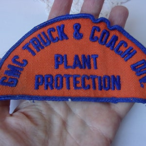 May include: A blue and orange embroidered patch with the text "GMC TRUCK & COACH DIV. PLANT PROTECTION"