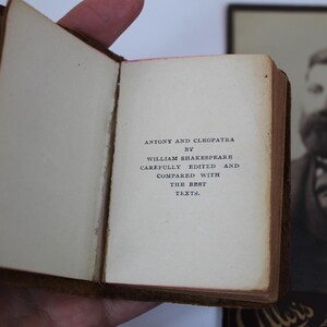 Peut inclure: Un petit livre ouvert avec le titre "Antony and Cleopatra" de William Shakespeare. Le texte est imprim&eacute; &agrave; l'encre noire sur des pages blanc cass&eacute;. Le livre est tenu ouvert, r&eacute;v&eacute;lant le texte, avec une couverture en cuir marron.