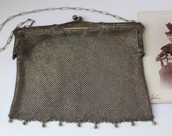 Peut inclure: Un sac à main en maille argentée avec une bandoulière chaîne et un fermoir décoratif. Le sac à main a une frange perlée en bas.
