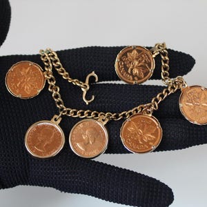 May include: A gold chain bracelet with multiple Canadian coins attached. The coins are all gold-toned and feature a maple leaf design.