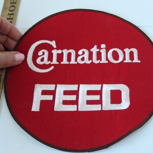 May include: A red circular patch with a white embroidered Carnation Feed logo.