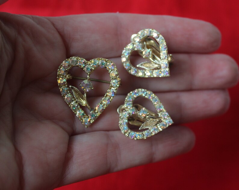 May include: A set of three gold-tone heart-shaped earrings with clear iridescent rhinestones and a floral design.