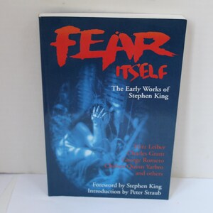 May include: A paperback book titled Fear Itself: The Early Works of Stephen King. The cover is dark blue with bold red text for the title. It features a blue-toned illustration of a figure with hands over their face and lists contributing authors.