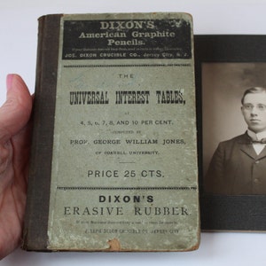 May include: A vintage book titled "Dixon's Universal Interest Tables" with the subtitle "At 4, 5, 6, 7, 8, and 10 Per Cent. Computed by Prof. George William Jones, of Cornell University." The book is priced at 25 cents.