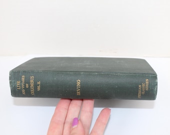 May include: A dark green hardcover book with gold lettering. The title is "Life and Voyages of Columbus" and the author is "Irving". The book is part of the "American Classic Series".