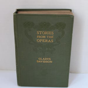 Puede incluir: Un libro antiguo de tapa dura, "Stories from the Operas" de Gladys Davidson. La cubierta es verde oscuro con letras doradas y detalles decorativos en relieve. Los bordes de las páginas son de color marrón claro.