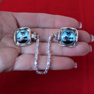May include: A pair of silver tone butterfly wing jewellery clips connected by a silver chain. The butterfly wings are blue with black markings and a small orange accent.