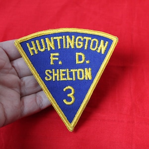 May include: A blue and gold triangular patch with the text "Huntington F.D. Shelton 3" embroidered on it.