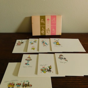 May include: A collection of vintage greeting cards and a box set. The cards feature floral and whimsical illustrations with phrases like "Happy Birthday" and "Thank you!" The box is pink with the words "Post a Note".