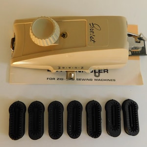 May include: A vintage beige and cream-colored Freist zig-zag sewing machine attachment with a dial and the brand name in script. Includes a set of seven black rubber attachments and a paper instruction sheet. The text on the sheet reads "FOR ZIG-ZAG SEWING MACHINES."