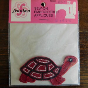 May include: A red and black embroidered turtle applique, packaged in a clear plastic sleeve. The packaging includes the brand name "franken" and the text "SEW-ON EMBROIDERED APPLIQUES". The turtle design features a segmented shell.