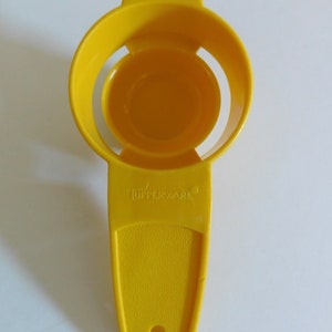 May include: A bright yellow Tupperware egg separator. The separator has a circular design with a handle and the Tupperware logo. The plastic has a textured surface and a small hole at the end of the handle.