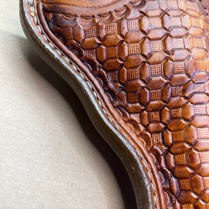 May include: A brown leather holster with a detailed geometric pattern. The holster is designed to hold a firearm.