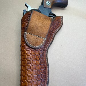 May include: A brown leather holster with a checkered pattern and a stitched border. A silver revolver is inside the holster.