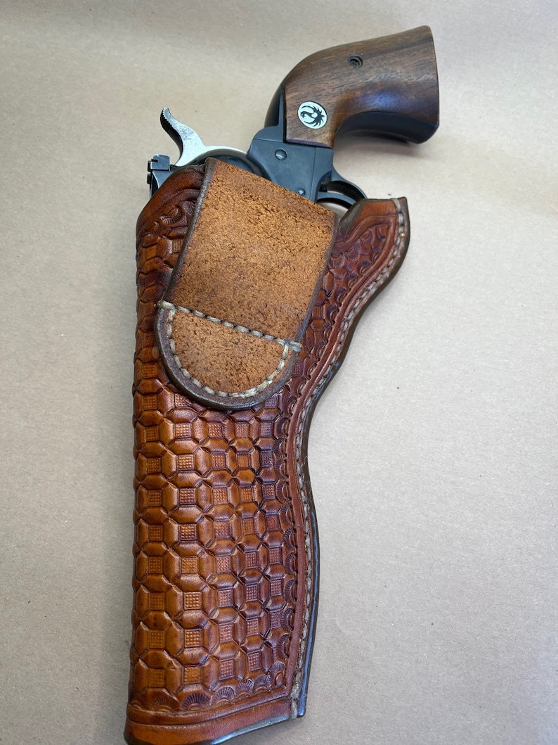 May include: A brown leather holster with a checkered pattern and a stitched border. A silver revolver is inside the holster.