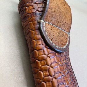 May include: A brown leather holster with a geometric pattern. The holster has a flap that folds over the top and secures with a snap.