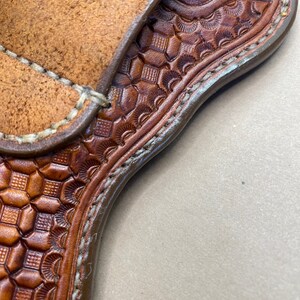 May include: A brown leather holster with a decorative pattern and stitching. The holster is designed to hold a firearm.