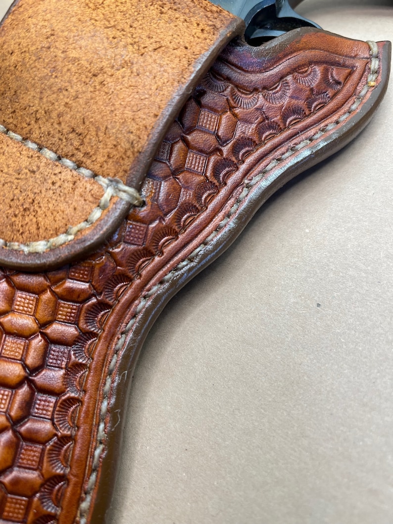May include: A brown leather holster with a decorative pattern and stitching. The holster is designed to hold a firearm.