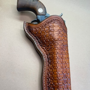 May include: A brown leather holster with a checkered pattern. A revolver is partially visible inside the holster.
