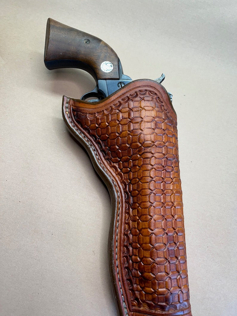 May include: A brown leather holster with a checkered pattern. A revolver is partially visible inside the holster.