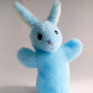 May include: A light blue plush bunny puppet with long ears and a white inner ear lining. The puppet has black eyes and a red nose.