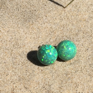 May include: A pair of green opal stud earrings with a sparkly finish. The earrings are round and have a silver backing.