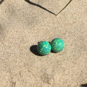 May include: A pair of green opal stud earrings with a shimmery finish. The earrings are round and have a smooth surface.