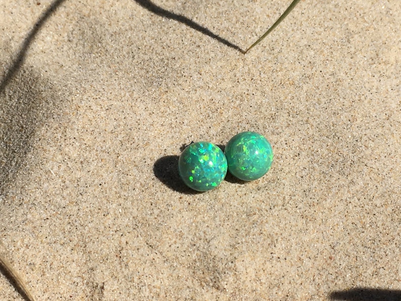 May include: A pair of green opal stud earrings with a shimmery finish. The earrings are round and have a smooth surface.