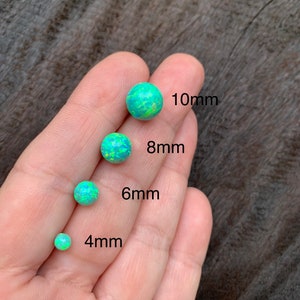 May include: Four opal cabochons in different sizes, 4mm, 6mm, 8mm, and 10mm. The opals are a light green color with a white and yellow iridescent sheen.