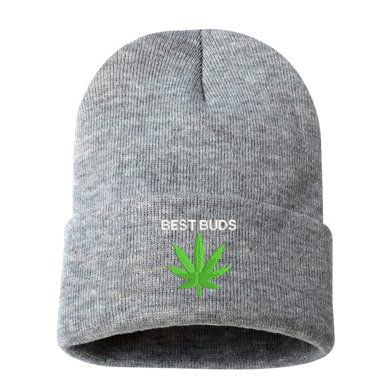 May include: A gray beanie with the embroidered text "BEST BUDS" in white above a green cannabis leaf. The beanie is made of a soft, knitted material.