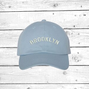 May include: A light blue baseball cap with the word "BROOKLYN" embroidered in white on the front.