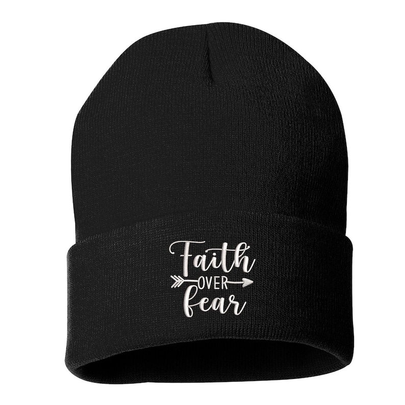 K&ouml;nnte beinhalten: Schwarze Beanie-M&uuml;tze mit dem Text "Faith over Fear" in wei&szlig;er Schrift und einem Pfeildesign. Die M&uuml;tze ist aus weichem Strickmaterial gefertigt und hat einen gefalteten Rand. Die Beanie ist ein Winteraccessoire.