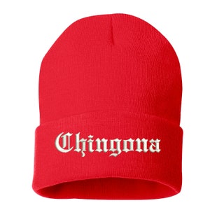 May include: A bright red beanie hat with the word "Chingona" embroidered in white script across the folded brim. The hat is made of a soft, knitted material and is designed to be worn on the head.