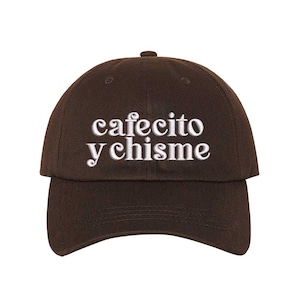 May include: A brown baseball cap with the embroidered text "cafecito y chisme" in white. The cap has a curved brim and a button on top. The hat is made of a soft fabric.