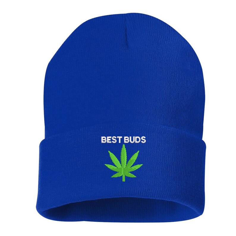 May include: A royal blue beanie with the words "BEST BUDS" in white, above a green cannabis leaf. The beanie is a solid color with a folded cuff.