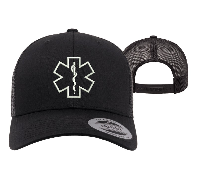 May include: Black trucker hat with a white embroidered medical symbol, the Star of Life, with a snake and staff. The hat has a black mesh back and a black adjustable snap closure. The hat has a label that says "The Classic Snapback, Tuff Stuff Since 1971."