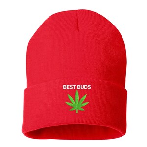 May include: A bright red beanie with the words "BEST BUDS" embroidered in white above a green cannabis leaf. The beanie is a classic, folded-brim style, perfect for casual wear.